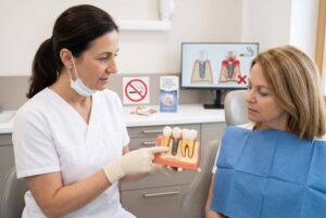 Dentista em Bauru explica riscos do implante dentário para fumantes usando modelo didático para uma paciente no consultório.